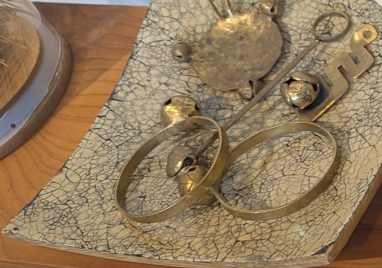 Brass bangles, a hammered brass disc and a brass stem with small bells on a cream crackle-glaze tray