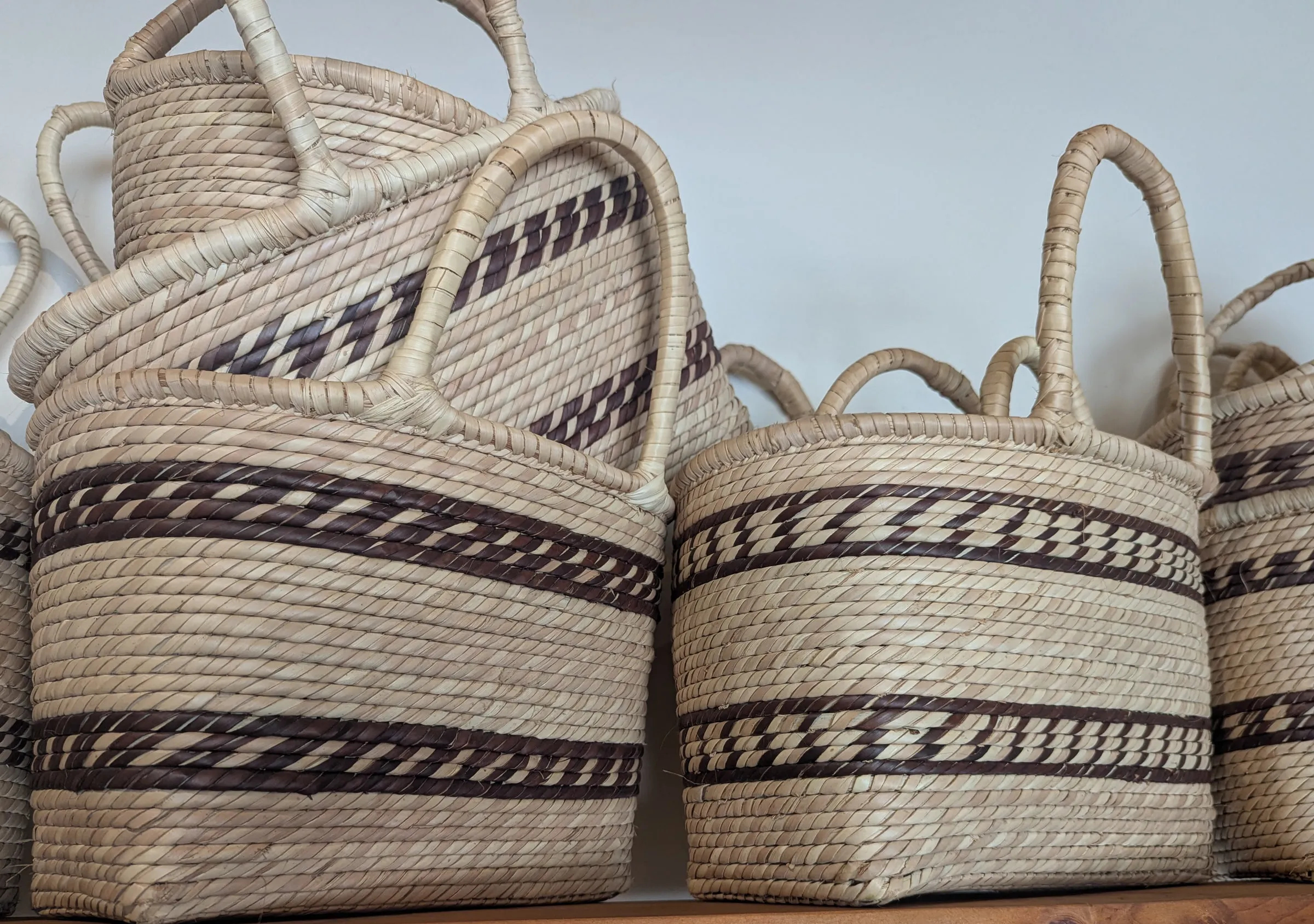 Stacked Ilala palm baskets with dark brown woven bands on a yellowwood shelf