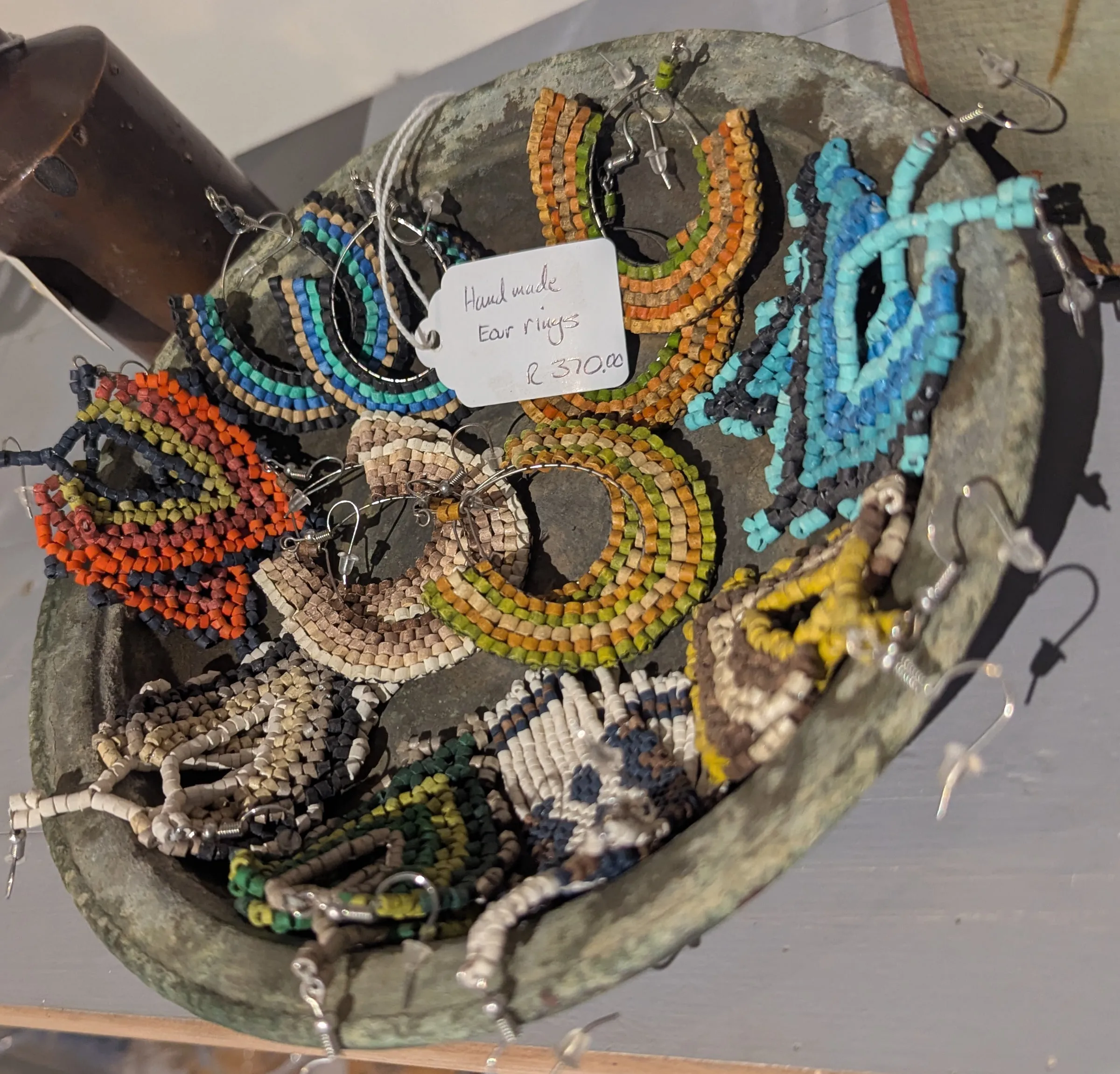 A verdigris bowl full of beaded hoop earrings in orange, turquoise, cream and black