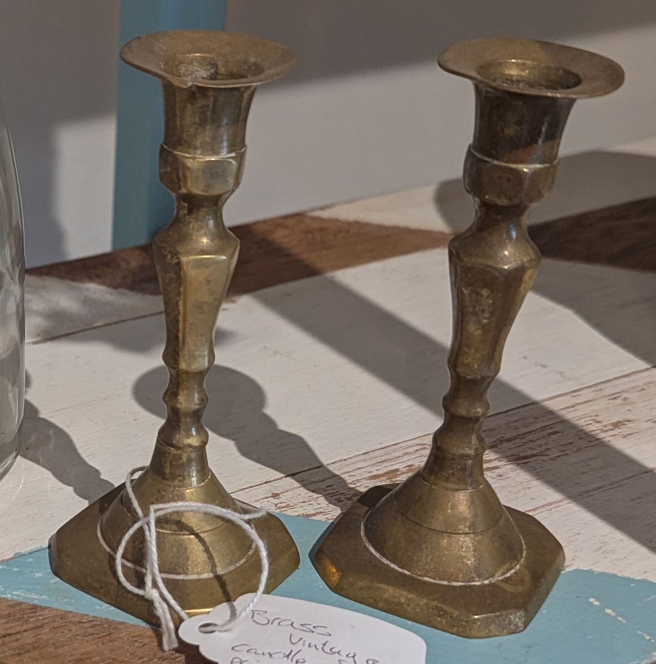A pair of vintage turned brass candlesticks on a painted wooden shelf