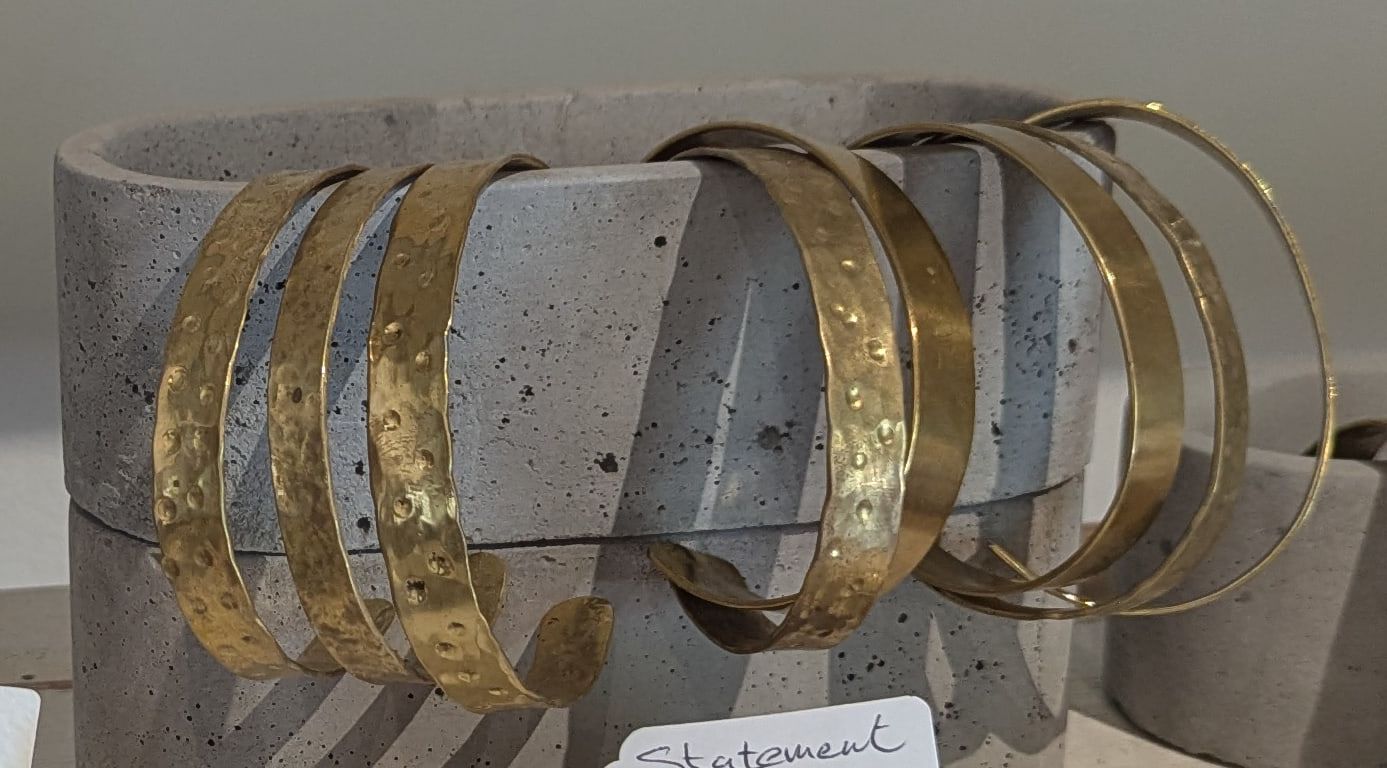 A row of broad hammered brass cuffs on a cast concrete stand