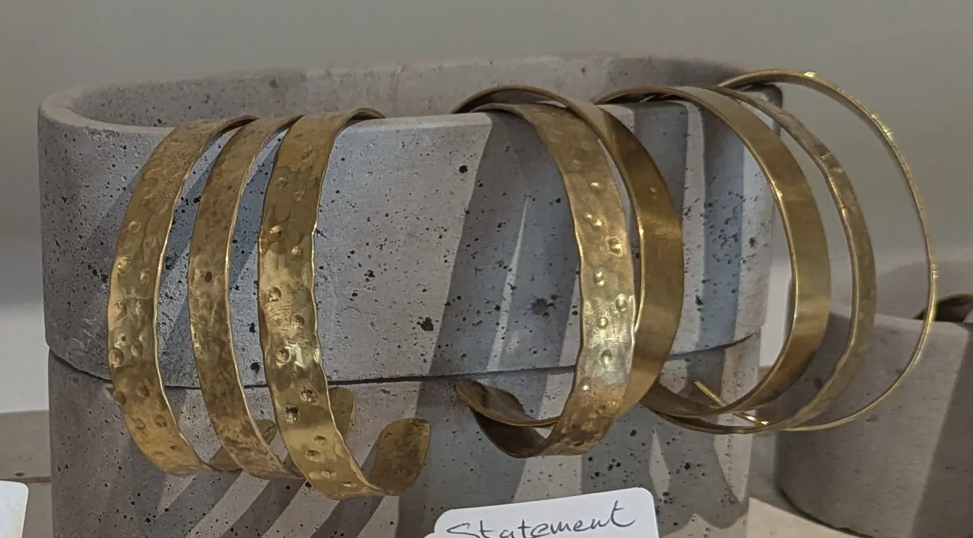 A row of broad hammered brass cuffs on a cast concrete stand
