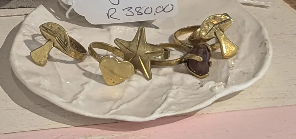 Brass rings topped with a star, a heart, a leaf and a mushroom on a white ceramic dish