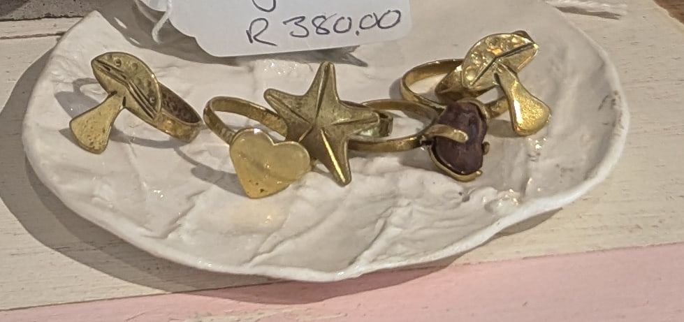 Brass rings topped with a star, a heart, a leaf and a mushroom on a white ceramic dish