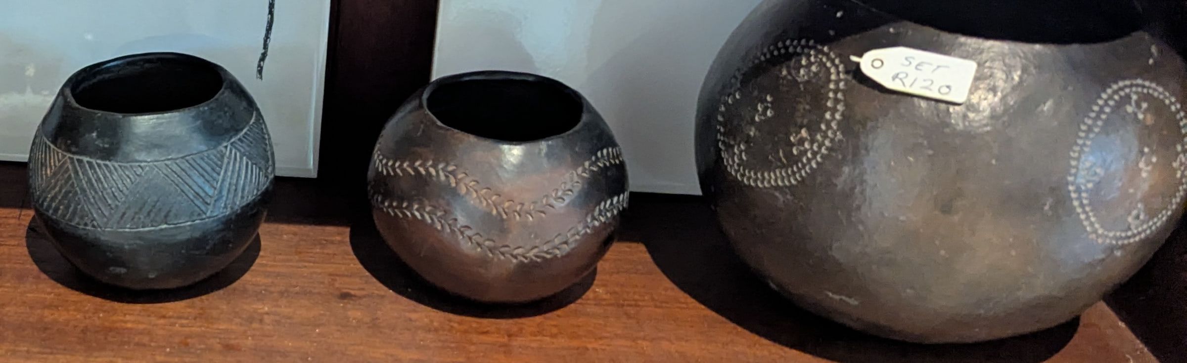 Three round burnished clay pots in black and brown with incised patterns