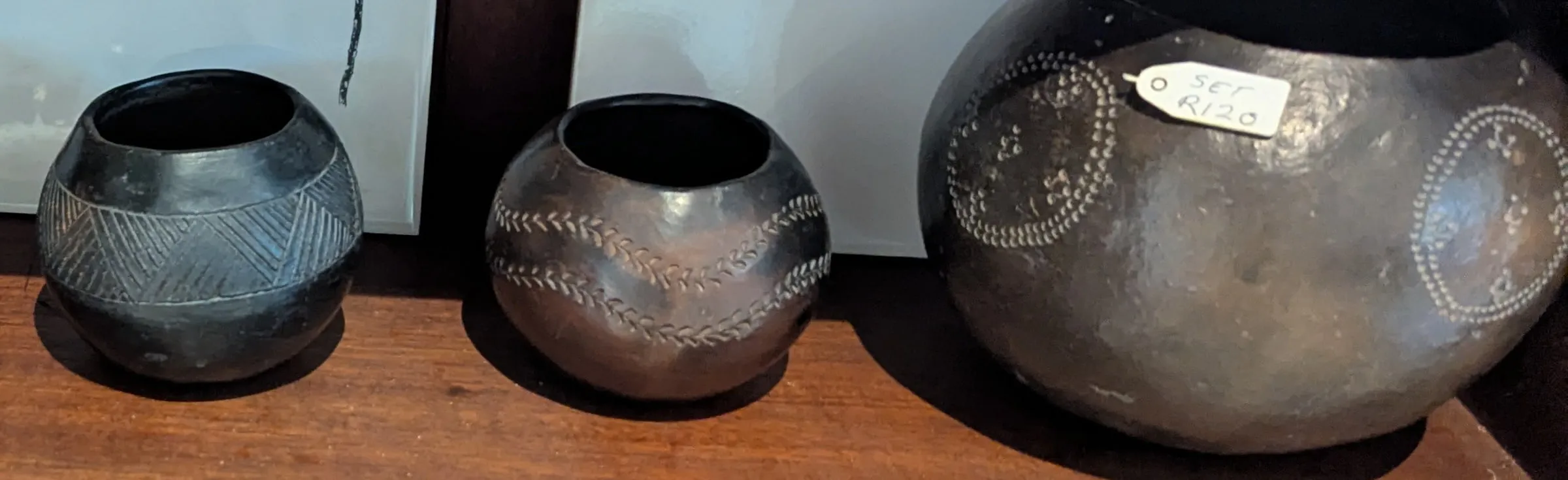 Three round burnished clay pots in black and brown with incised patterns