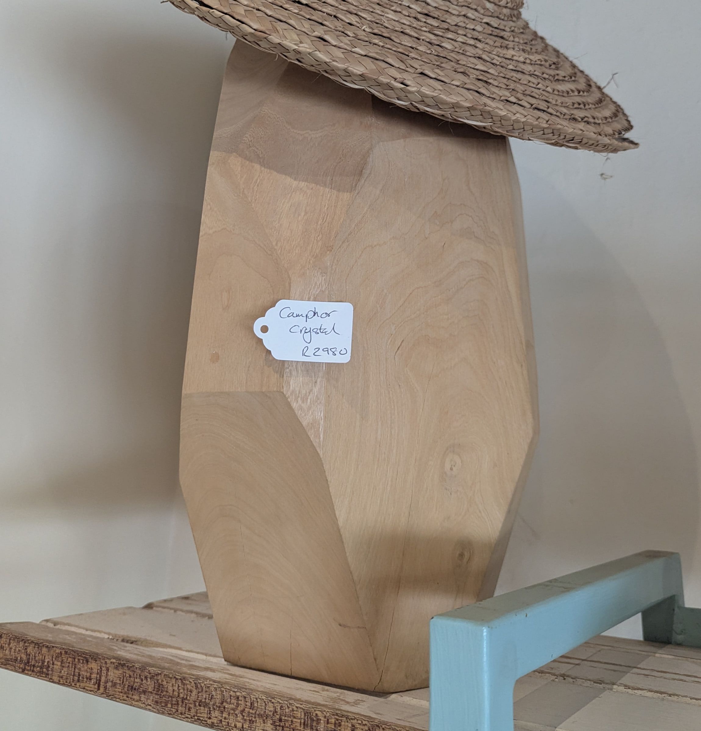 A tall faceted sculpture in pale camphor wood shaped like a crystal, with an Ilala hat resting on top