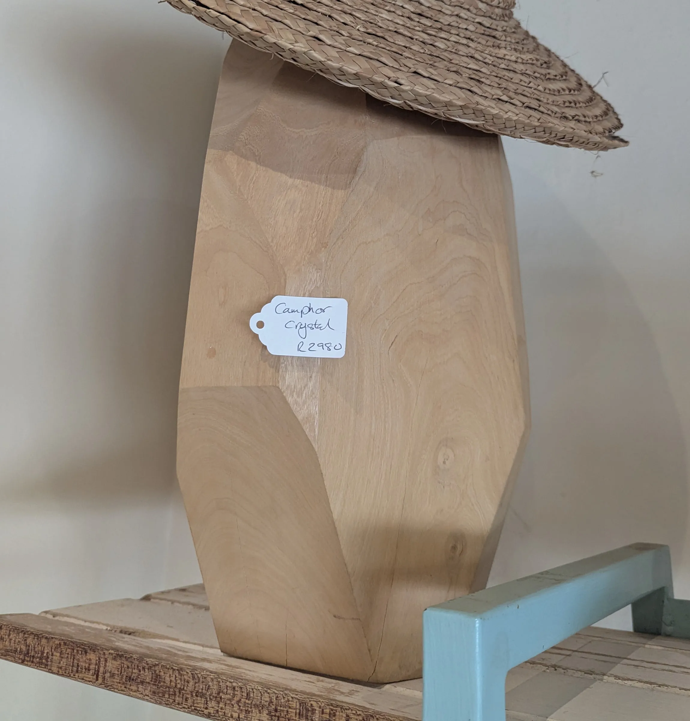 A tall faceted sculpture in pale camphor wood shaped like a crystal, with an Ilala hat resting on top
