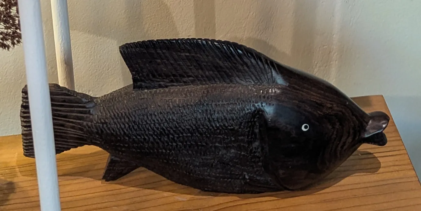 A dark hand-carved wooden fish on a yellowwood shelf