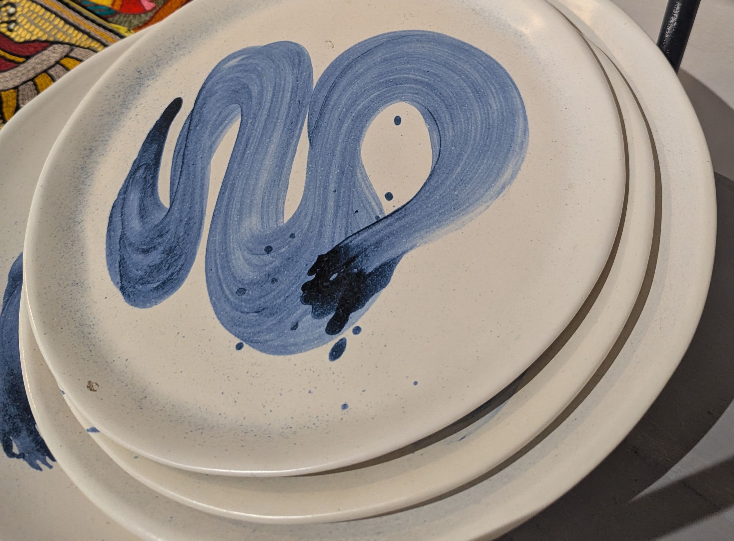 A stack of cream ceramic plates with a loose blue brushstroke swirl on the top plate