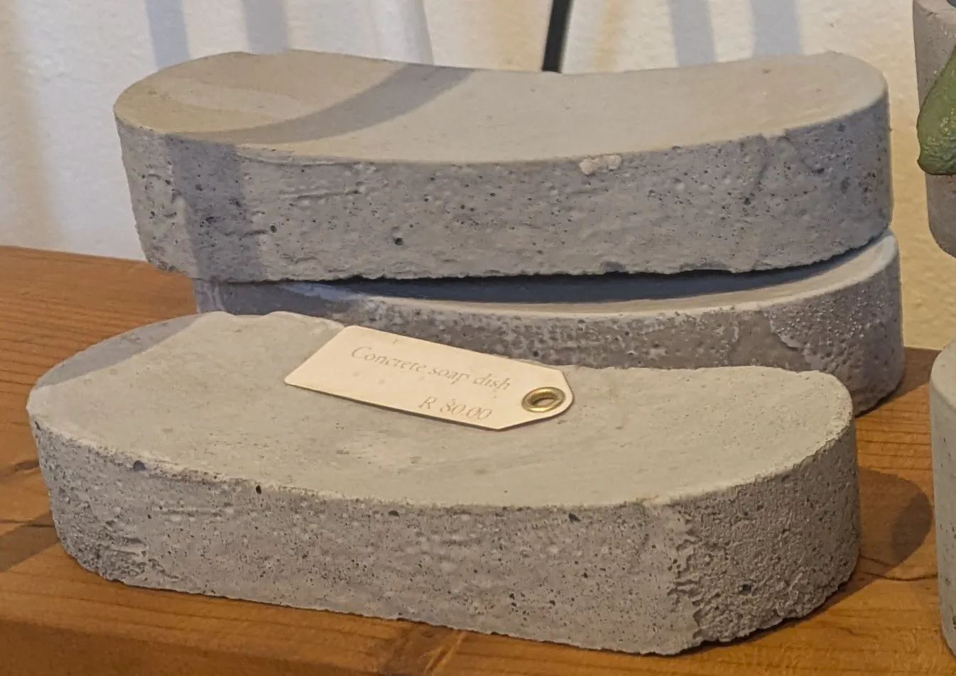 Curved grey concrete soap dishes stacked on a wooden shelf