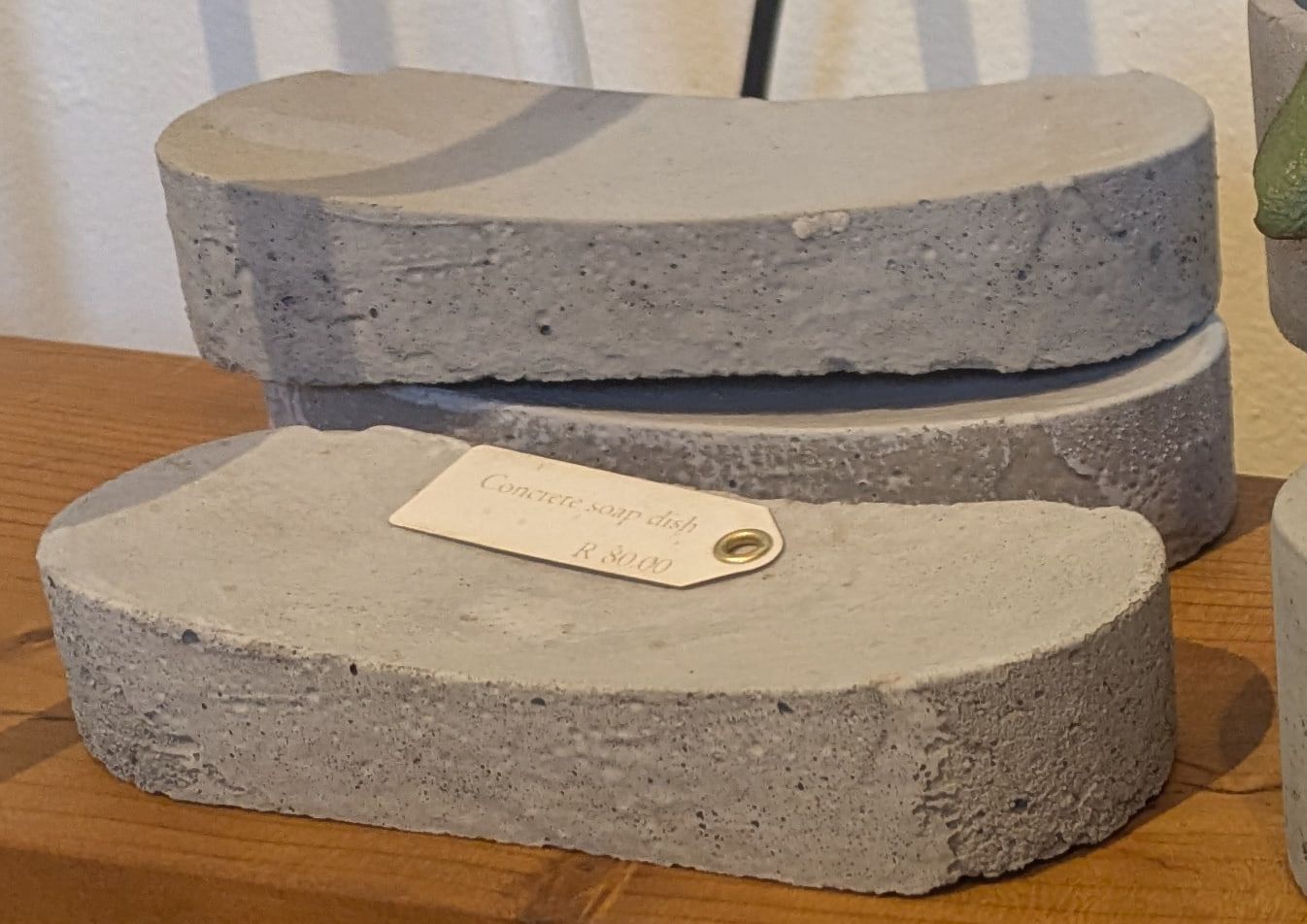 Curved grey concrete soap dishes stacked on a wooden shelf