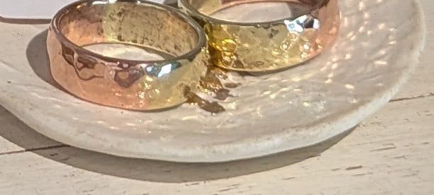Two wide rings in copper and brass on a white ceramic dish
