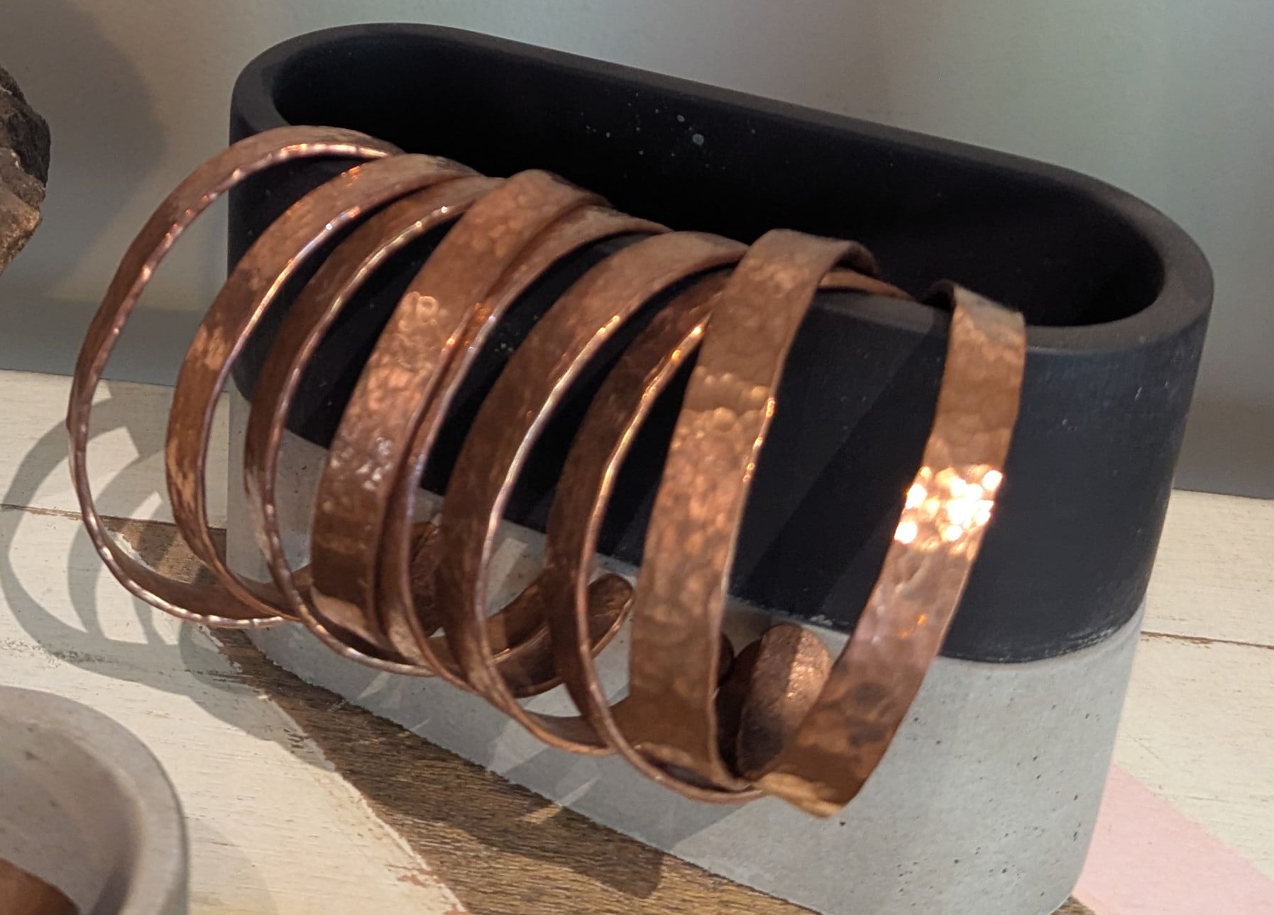 Hammered copper cuffs stacked over a black and concrete stand