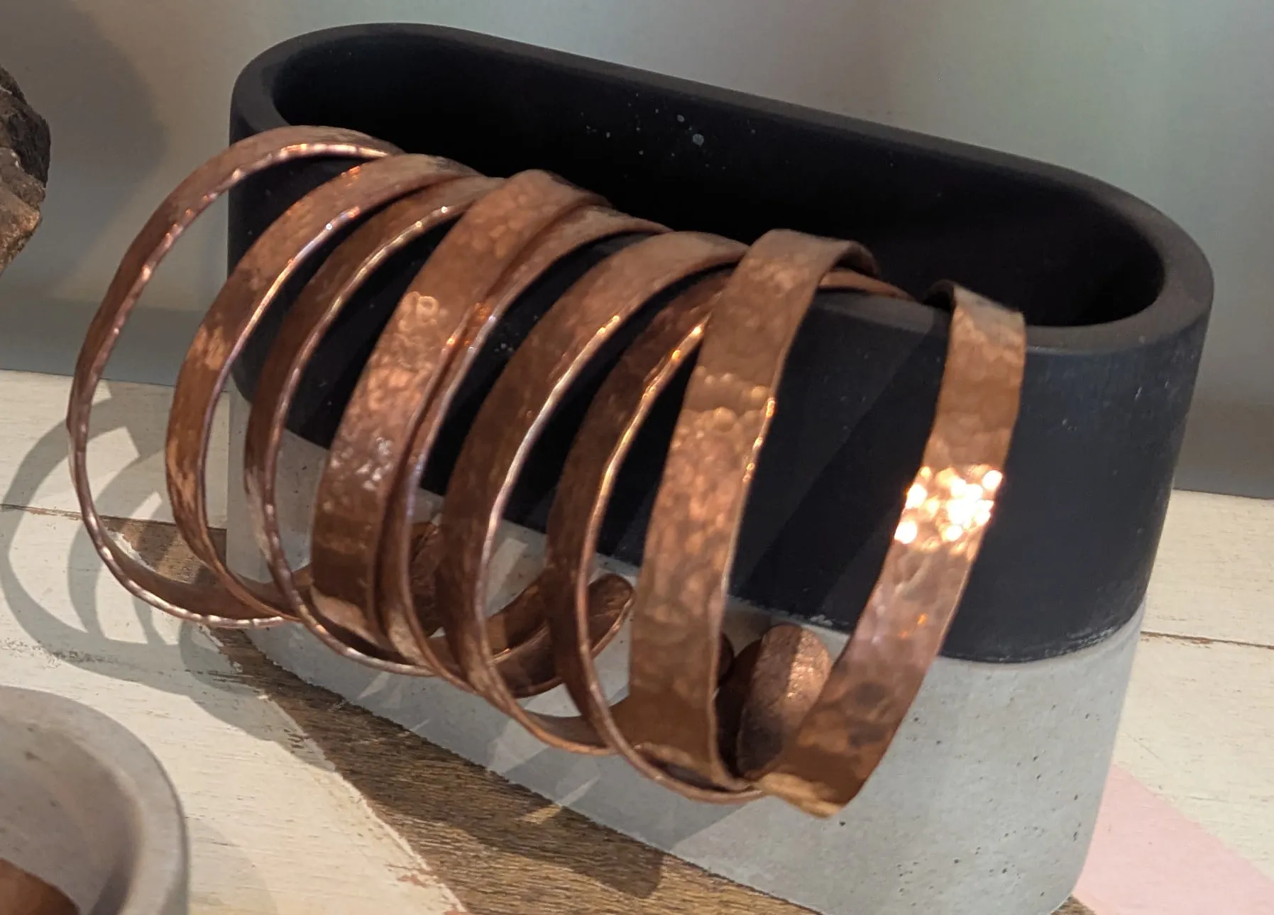 Hammered copper cuffs stacked over a black and concrete stand
