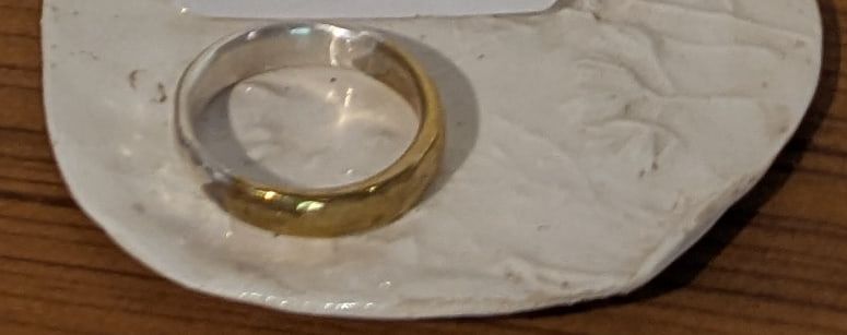 A two-tone ring in brass and silver on a white ceramic dish