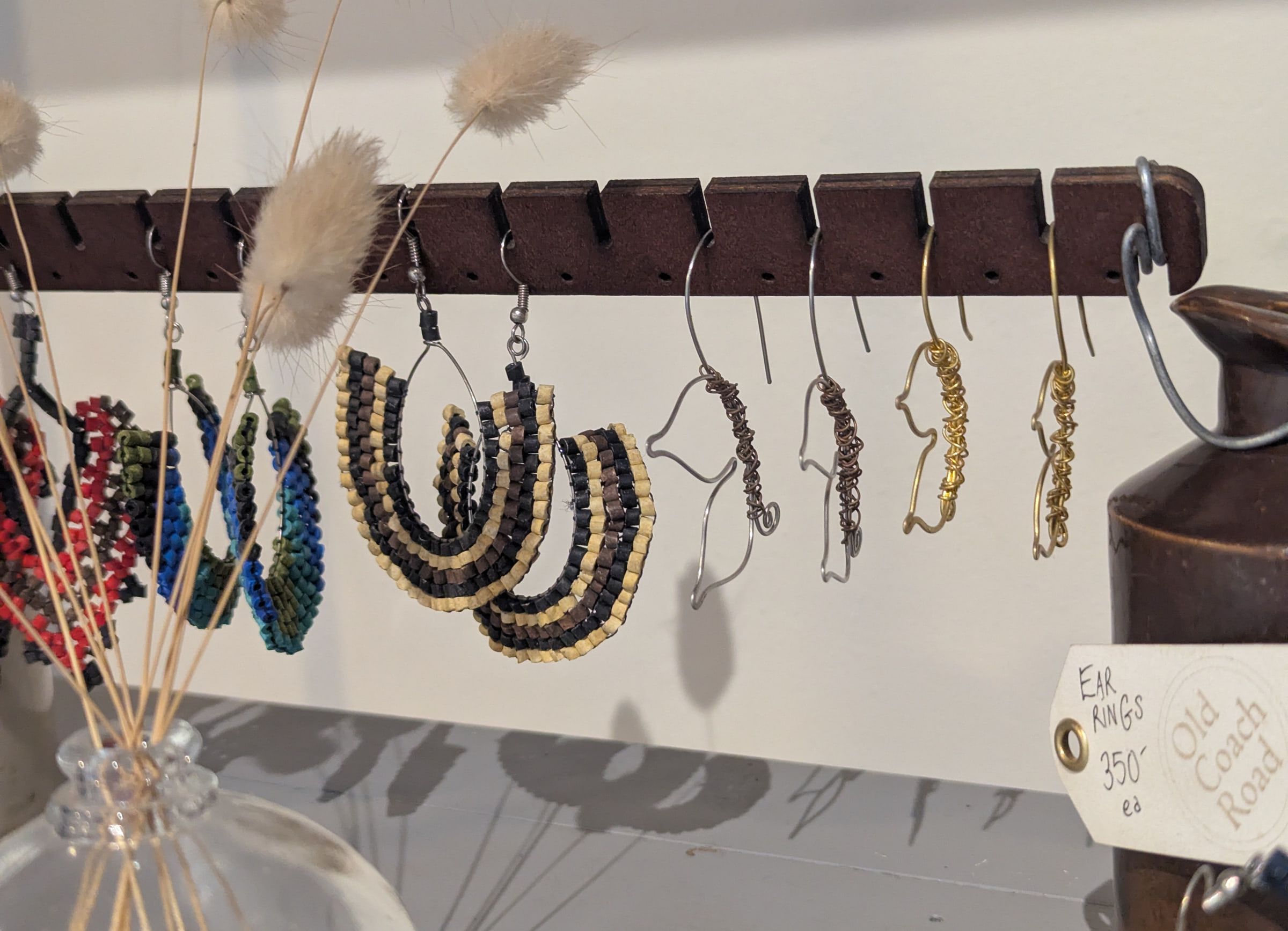 Wire and beaded earrings on a wooden bar with an Old Coach Road tag