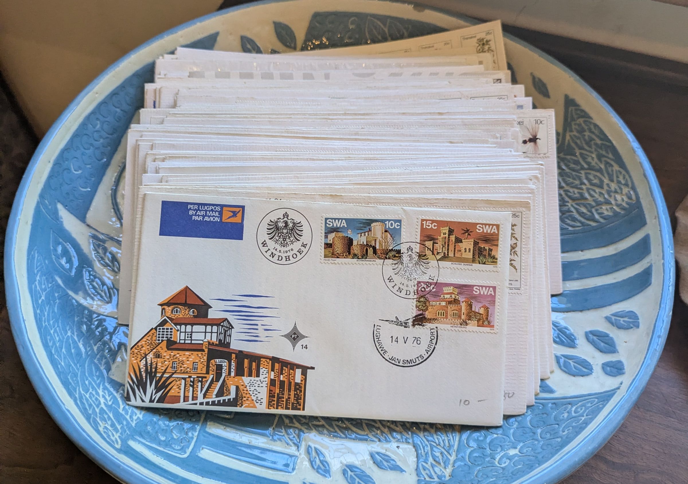 A stack of vintage first day covers with 1976 South West Africa stamps on a blue carved platter