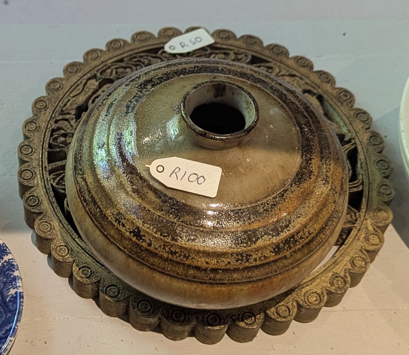 A round green and brown glazed stoneware vase on an ornate cast trivet