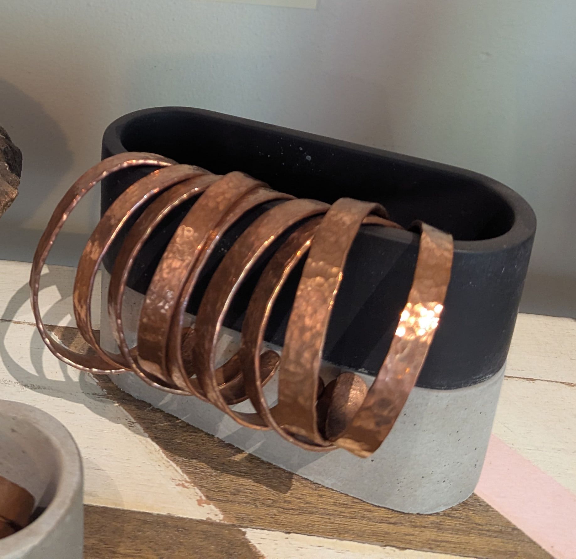 Hammered copper cuffs stacked on a black and concrete stand