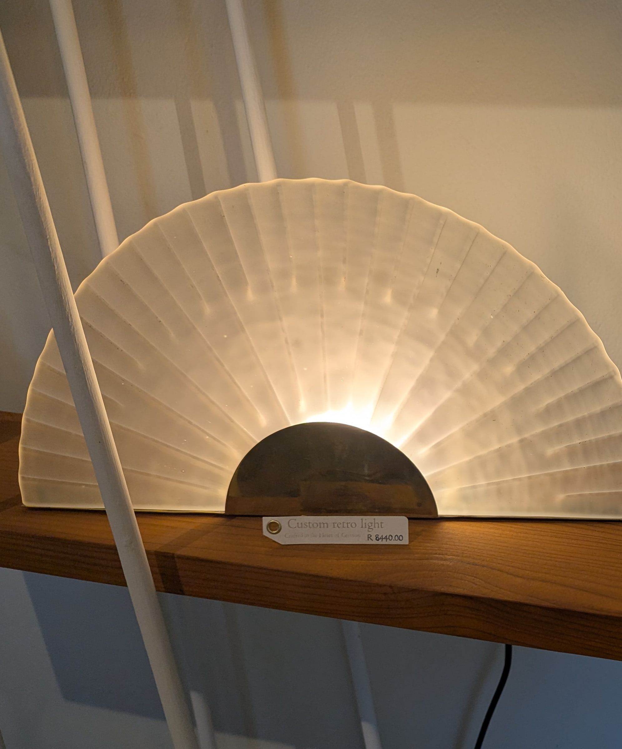 A fan of frosted fluted glass glowing above a brass half-moon base