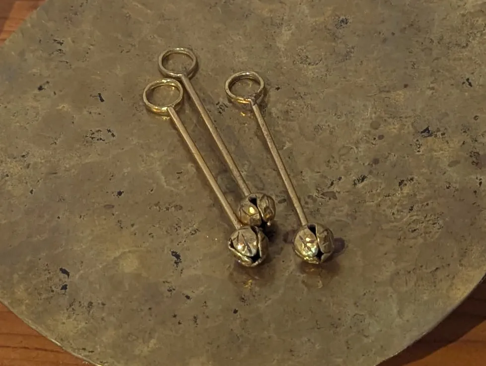 Three brass pendants with loops at the top and bud-shaped bells at the ends, lying on a hammered brass plate