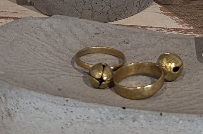 Two slim brass rings, each with a small round brass bell, resting on a cast concrete dish