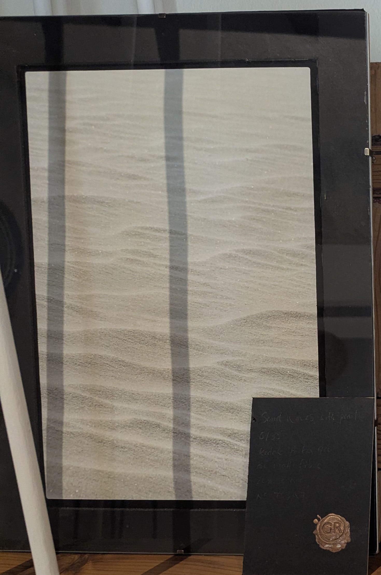 A framed photograph of fine sand ripples in a black frame