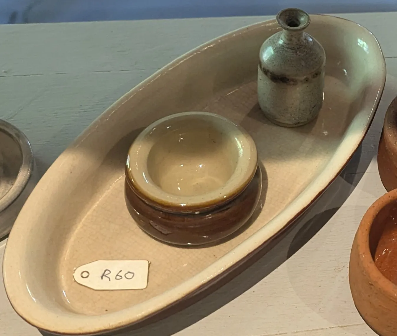 A long oval cream stoneware dish holding a small brown glazed bowl and bud vase