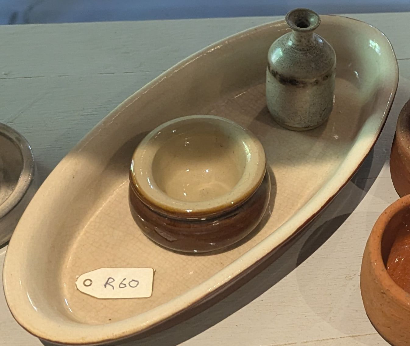 A long oval cream stoneware dish holding a small brown glazed bowl and bud vase