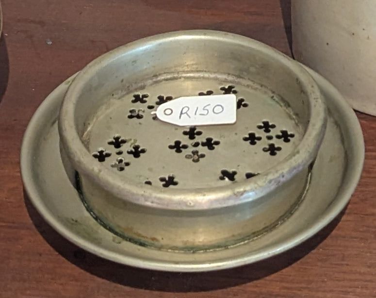 A round pewter soap dish with a pierced clover-pattern insert