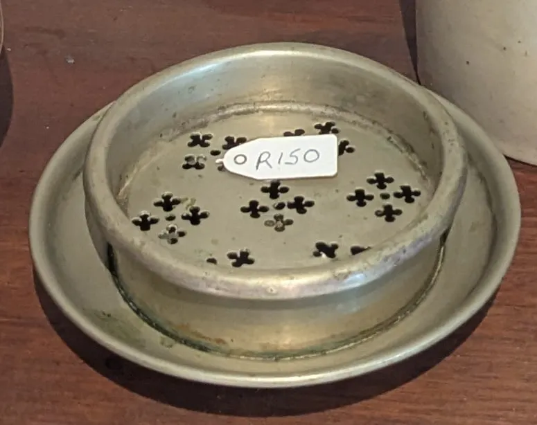A round pewter soap dish with a pierced clover-pattern insert