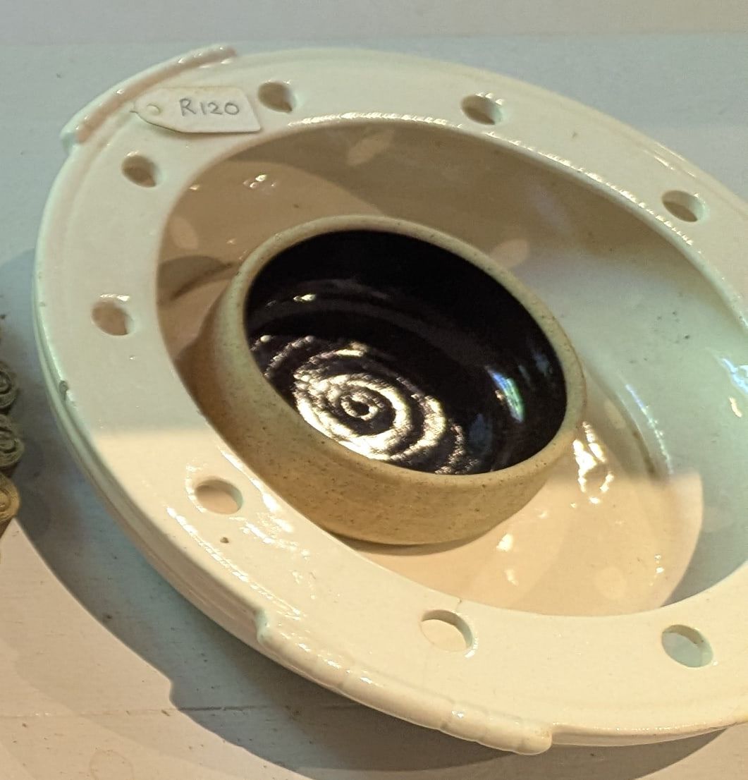 A white ceramic dish with round holes around the rim and a dark glazed centre