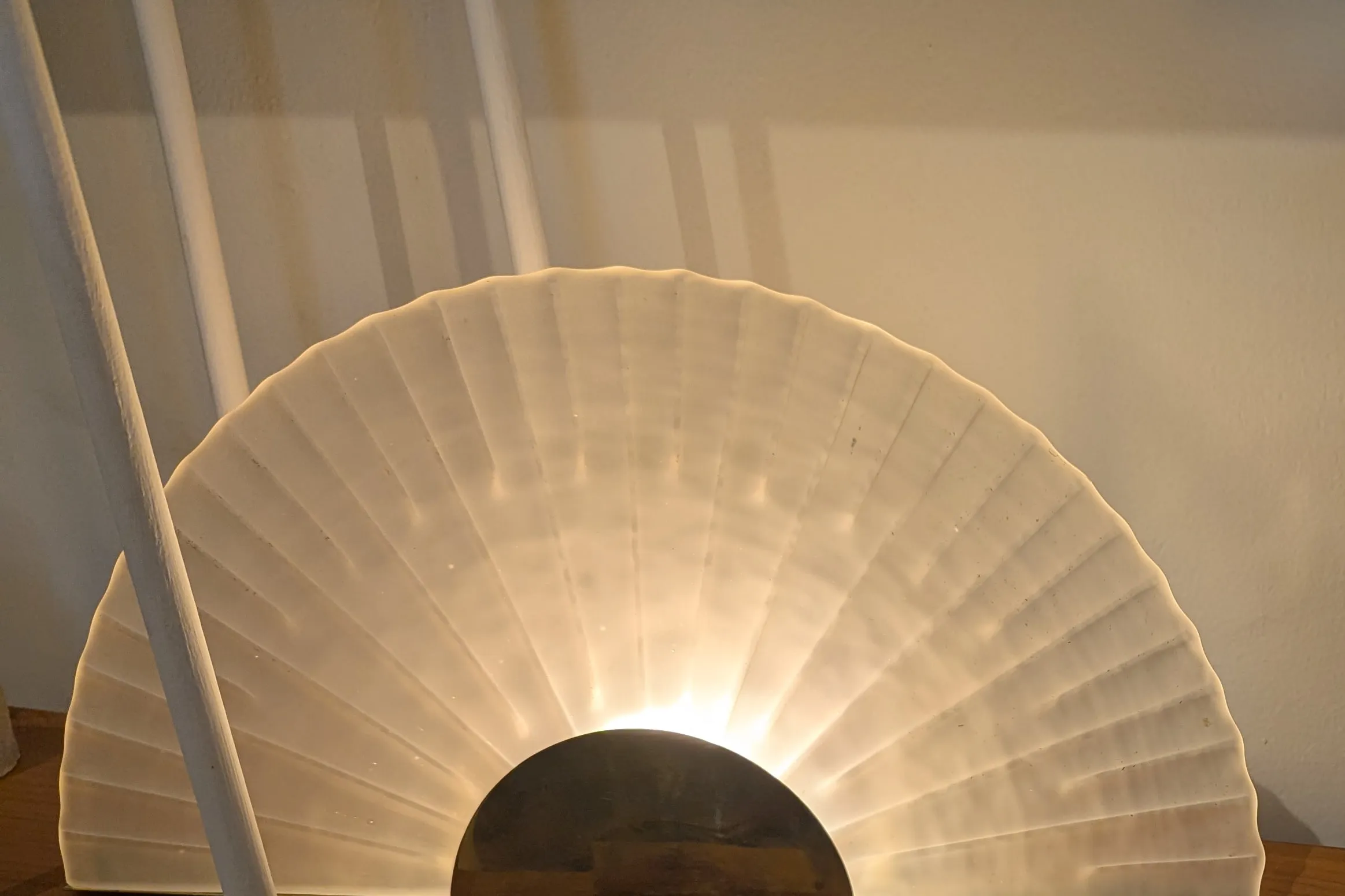 A fan-shaped frosted glass lamp on a brass half-moon base, glowing warm on a wooden shelf