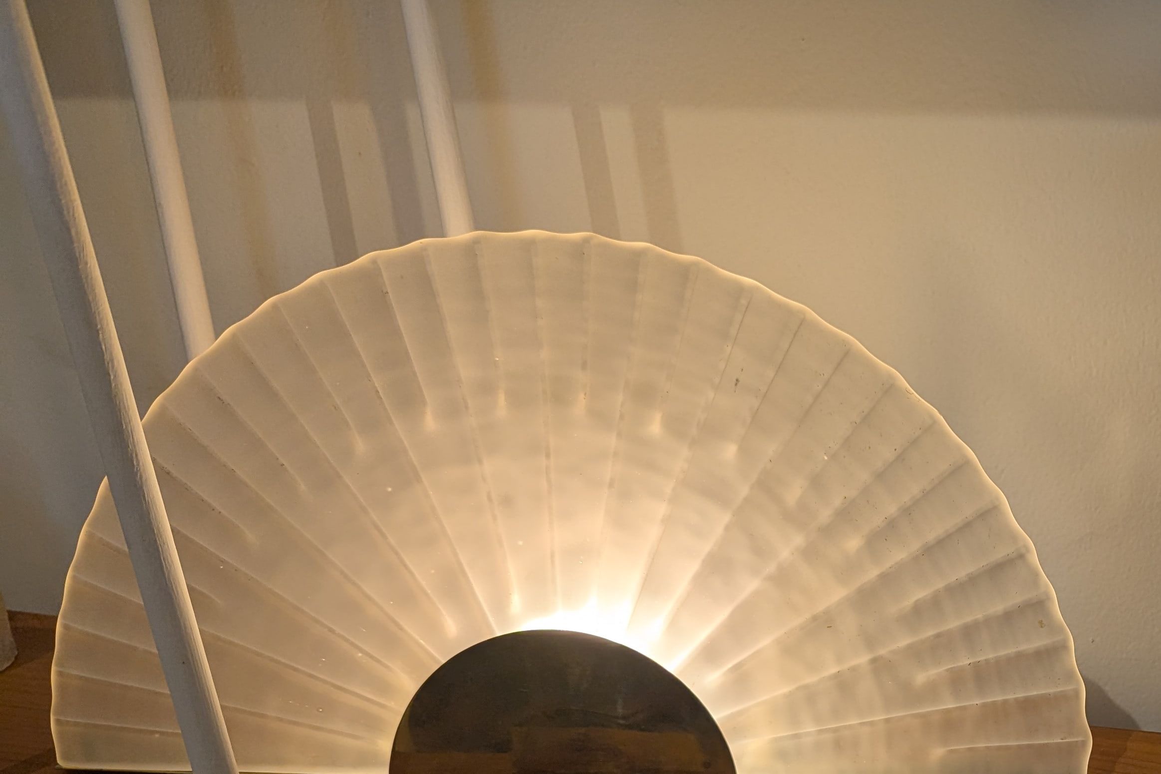 A fan-shaped frosted glass lamp on a brass half-moon base, glowing warm on a wooden shelf