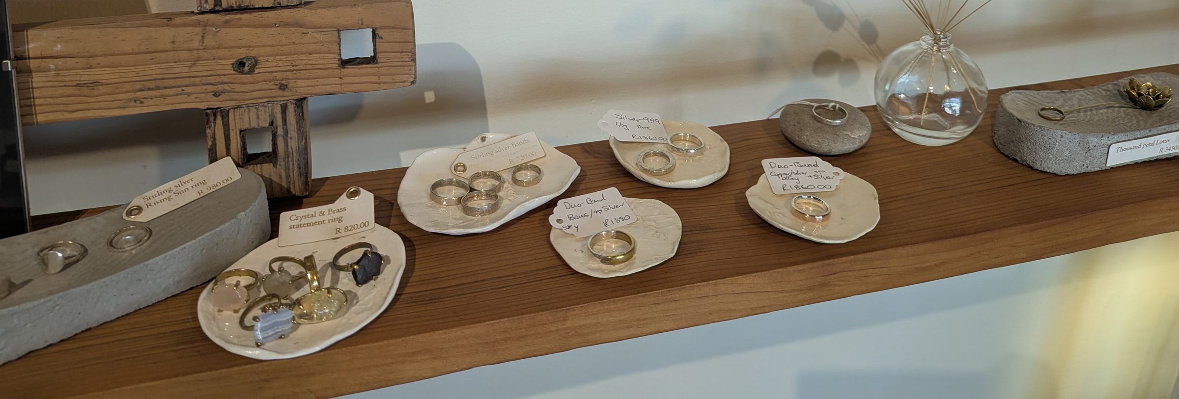 Silver and brass rings on white ceramic dishes along a shelf