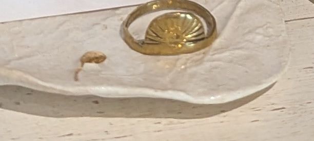 A brass ring with a half-sun motif on a white ceramic dish