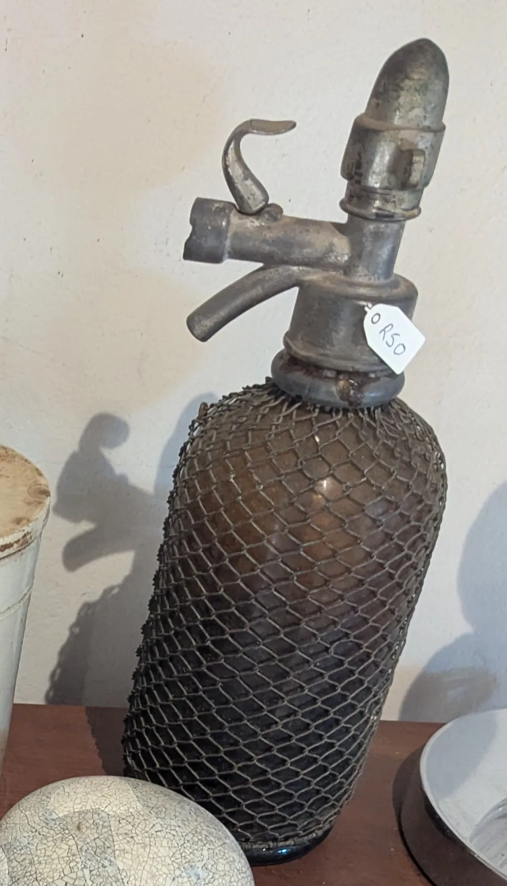 A vintage soda siphon in brown glass with wire mesh and a metal head