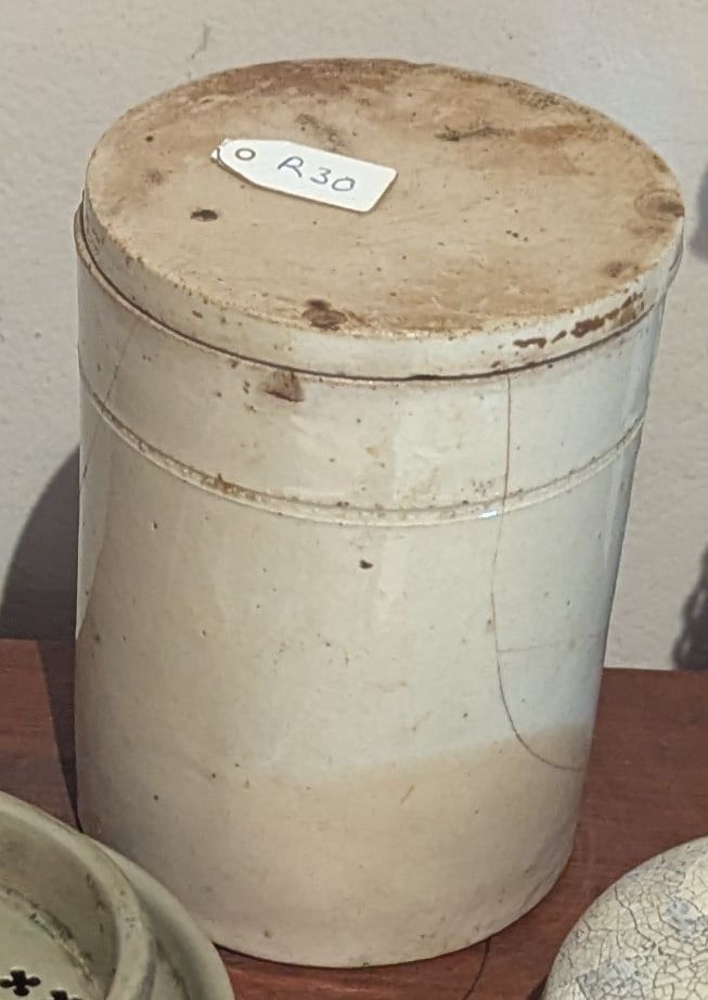 A tall cream stoneware crock with a worn glaze