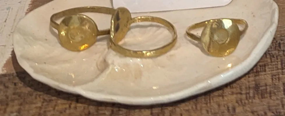 Three brass rings with round sun-shaped faces on a white ceramic dish