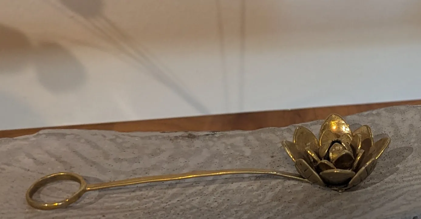 A brass lotus flower with layered petals on a long curved brass stem with a loop at the end