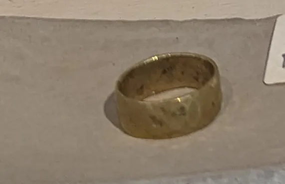 A wide hammered brass band ring resting on a concrete dish