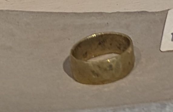 A wide hammered brass band ring resting on a concrete dish